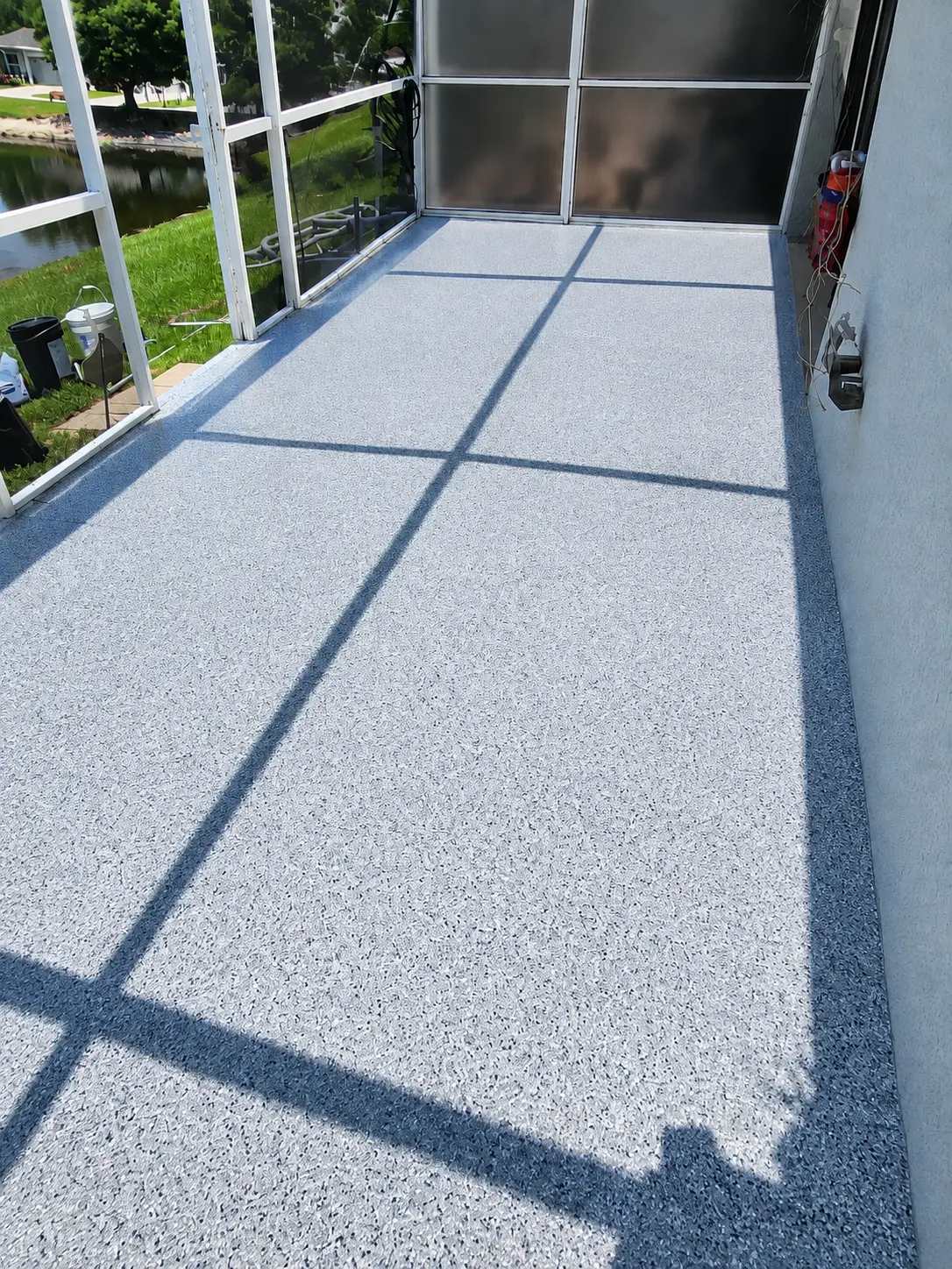 The same screened lanai with a fresh, even resurfaced patio floor and clean edges, with grass and water visible through the screen enclosure